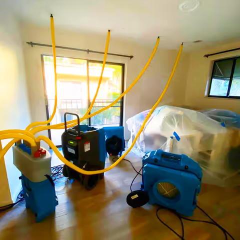 Air movers and a dehumidifier set up to dry a room with a wood floor