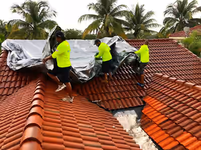 RestoPro770 crew in high-visibility shirts unrolling a silver tarp over a red barrel-tile roof