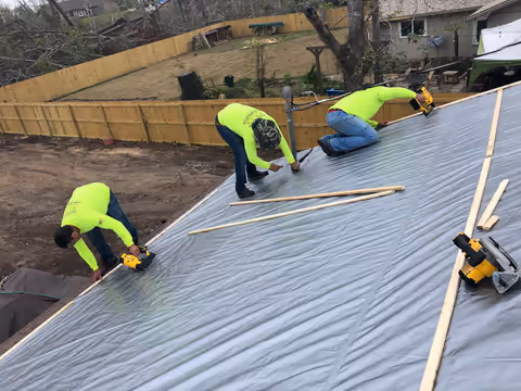 Two crew members in high-visibility shirts fastening a tarp with wood battens
